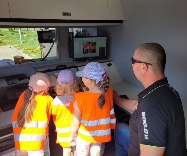 Dzieci i pracownik wodociągów przy ekranie moitopra w specjalistycznym samochodzie do filmowania wnętrza sieci kanalizacyjnej.