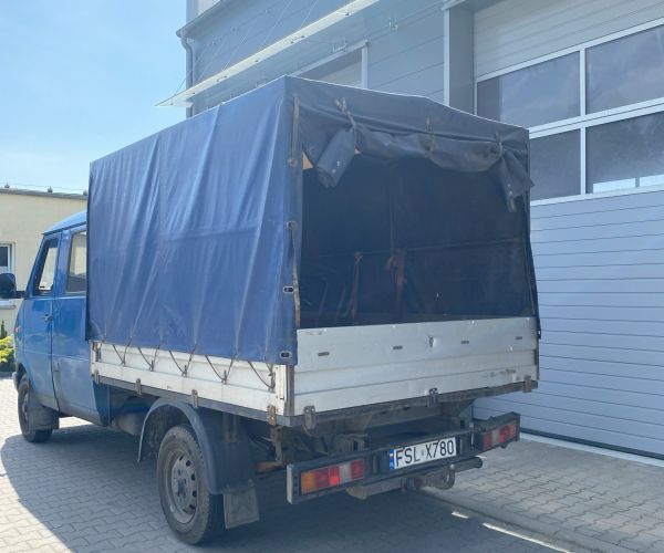 Samochód ciężarowo -osobowy marki lublin stojący przed wjazdem do garażu, widoczny tył przestrzeni ładunkowej z plandeką. 
