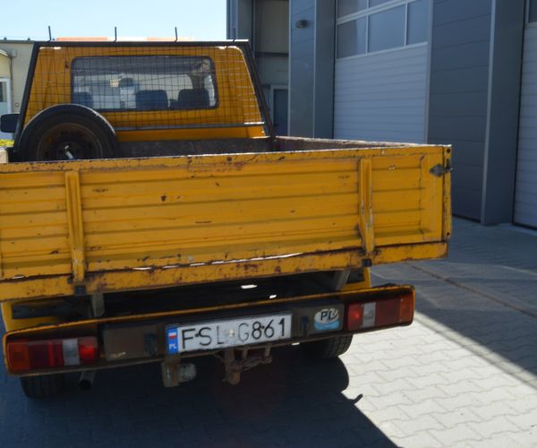 Samochód marki Volkswagen Transporter w kolorze żółtym na tle budynku Zakładu Usług Wodno-Ściekowych w Słubicach - widok z tyłu.