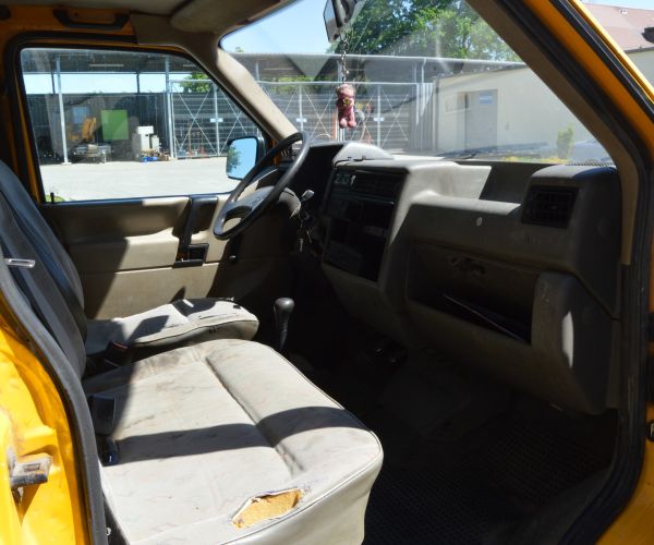 Samochód marki Volkswagen Transporter w kolorze żółtym na tle budynku Zakładu Usług Wodno-Ściekowych w Słubicach - widok wnętrze pasażerskie obok kierowcy. 