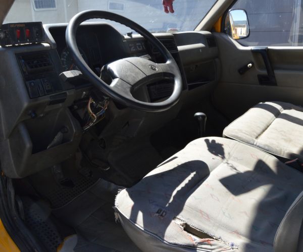 Samochód marki Volkswagen Transporter w kolorze żółtym na tle budynku Zakładu Usług Wodno-Ściekowych w Słubicach - widok fotel kierowcy i kierownica.