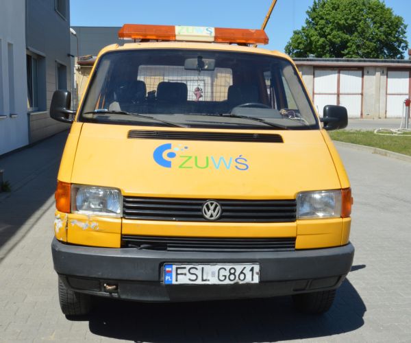 Samochód marki Volkswagen Transporter w kolorze żółtym na tle budynku Zakładu Usług Wodno-Ściekowych w Słubicach- widok z przodu. 